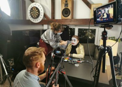 Woman touching up makeup on a woman dressed as a clown with the camera man in front