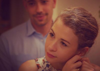 a man stands behind a woman and looks on as she puts on her earring