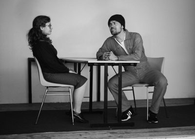 woman and man on stage sitting across from each other at a table